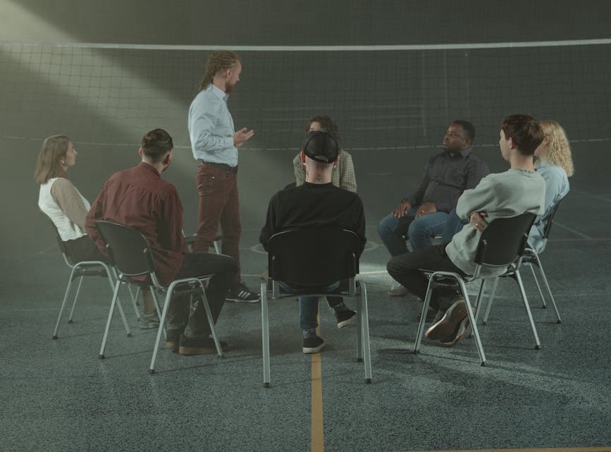 Group of diverse individuals sitting in a circle, engaging in a discussion, with a therapist facilitating the conversation, representing the supportive and collaborative environment of relationship therapy at Onesta Therapy Co.