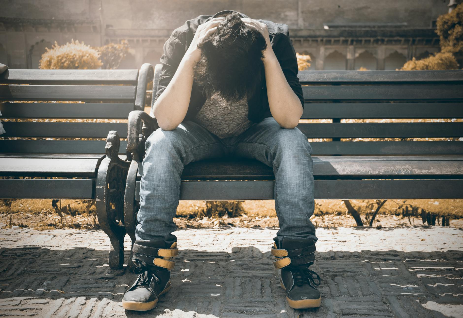 A person sitting on a park bench, holding their head in their hands, depicting the emotional and physical toll of chronic pain.