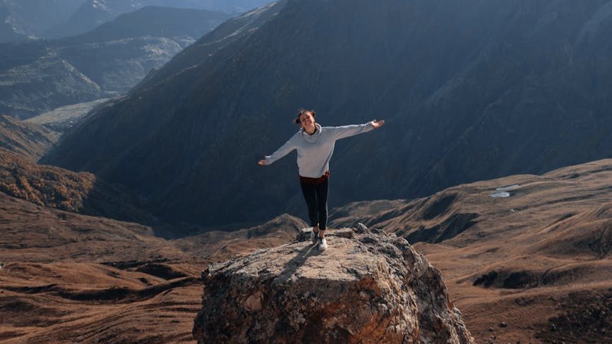 Person standing atop mountain, arms outstretched toward sky, symbolizing empowerment and overcoming obstacles.