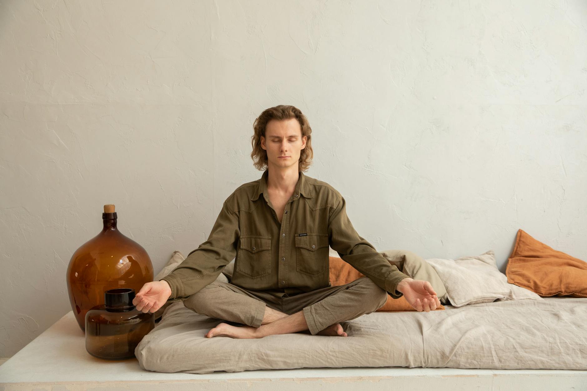 Person meditating in tranquil indoor space, sitting cross-legged with eyes closed, surrounded by soft light and calm atmosphere.