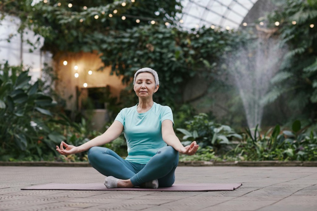 Person sitting on a yoga mat in a meditative pose, surrounded by greenery and natural light, symbolizing mindfulness meditation as a coping technique for chronic pain management.