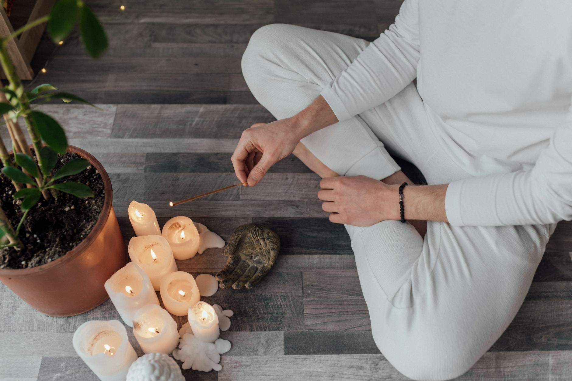 Person sitting in meditation surrounded by candles and incense.